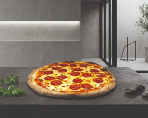 Pizza pepperoni sur une table moderne avec des herbes fraîches à côté.